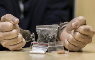 hand with handcuffs facing bags of drugs - Drug traffic charges in Georgia
